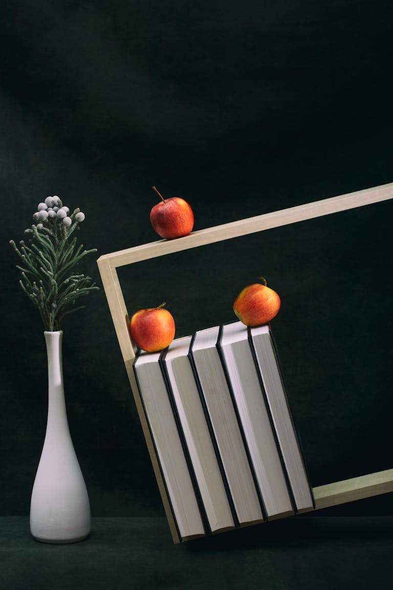 A creative still life featuring apples, books, and a vase for an artistic touch.