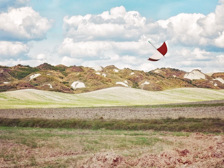 A picturesque view of Tuscany's rolling hills with a dramatic sky and an umbrella in flight.